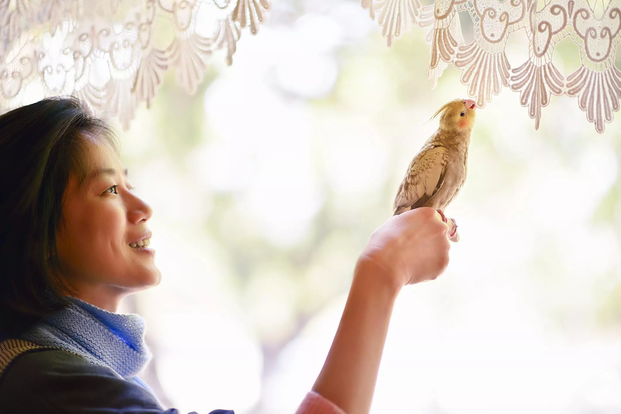 Cheerful woman and pet bird perched on her finger